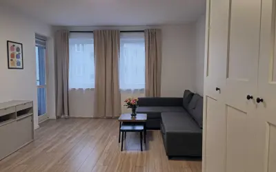 Nowoczesny salon z szarą kanapą, stolikiem kawowym z kwiatami i dużymi oknami.