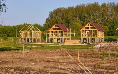 Trzy drewniane szkielety budynków gospodarczych na betonowych fundamentach, w tle drzewa.
