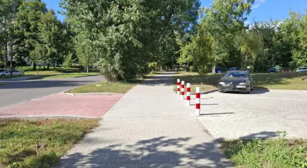 Chodnik z kostki brukowej, słupki parkingowe, samochód i drzewa w słoneczny dzień.