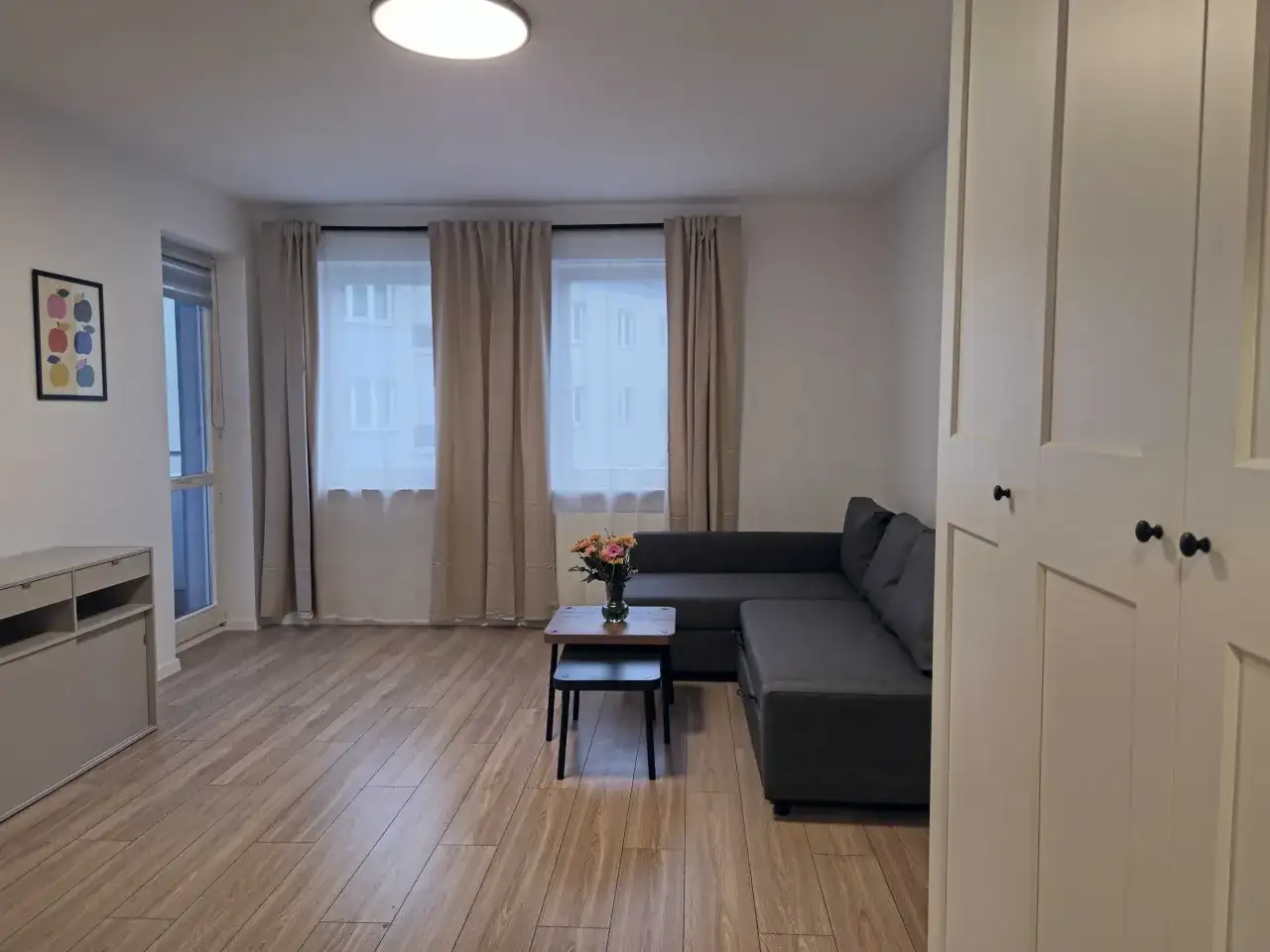 Nowoczesny salon z szarą kanapą, stolikiem kawowym z kwiatami i dużymi oknami.